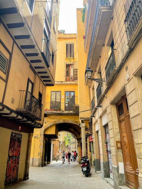 A narrow street in Barcelona's Gothic Quarter with warm stone buildings and a scooter parked by the wall