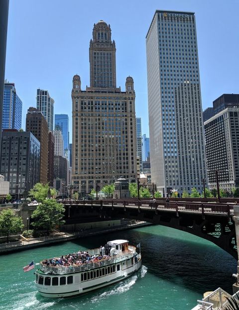 A tour boat full of passengers passing under a bridge on the Chicago River between tall buildings