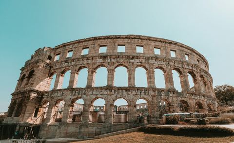 The Roman amphitheatre in Pula, its two tiers of stone arches against a pale sky