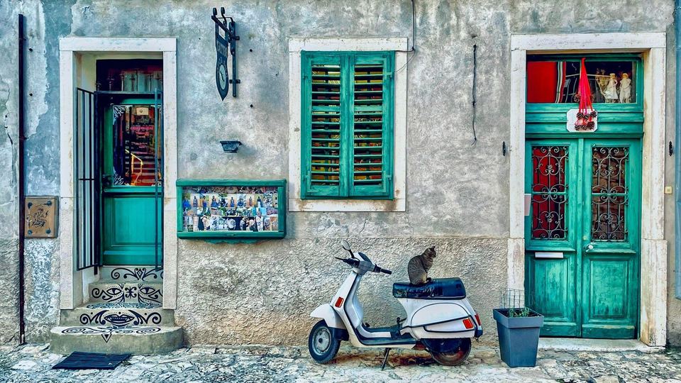 A cat sitting on a white Vespa outside green-shuttered doors in Rovinj's old town