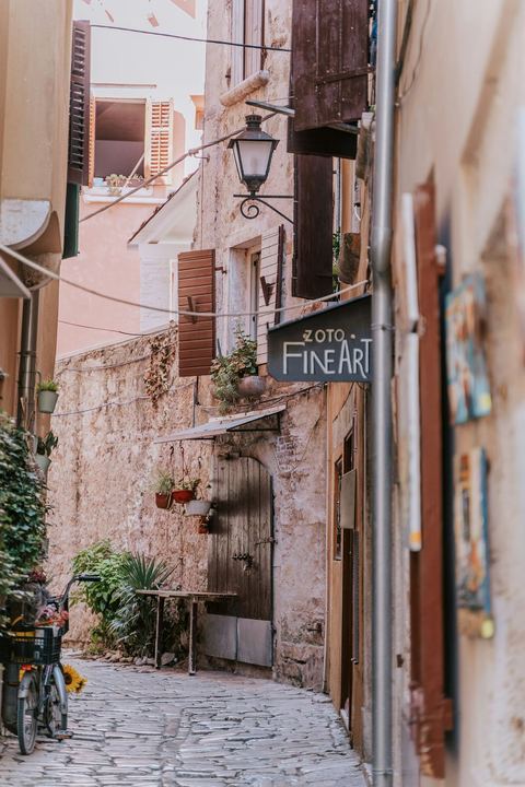 A narrow stone lane in Rovinj's old town with pastel walls and a hanging shop sign